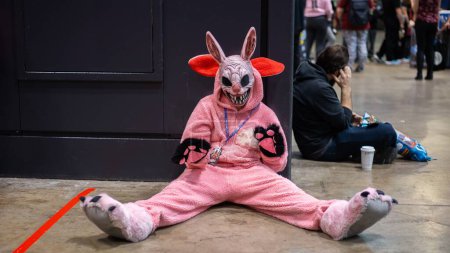 Foto de Una persona en traje rosa de un conejo con máscara de conejo de miedo sentado en el suelo - Imagen libre de derechos