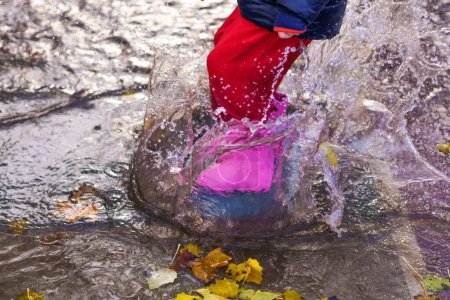 Foto de Child splashing water with boots and water pants in a puddle on a rainy day - Imagen libre de derechos