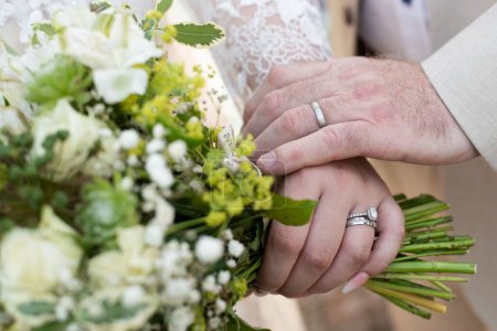 Foto de Un primer plano de las manos del novio y la novia con anillos y un ramo en el día de su boda - Imagen libre de derechos