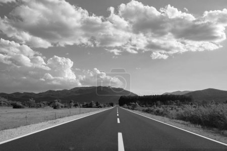 Téléchargez les photos : Une vue en niveaux de gris de la route de campagne ouverte avec des montagnes et des herbes - en image libre de droit