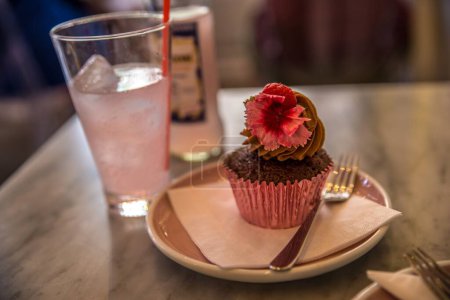 Photo for A closeup of a chocolate cupcake with pink flower on a table with juice - Royalty Free Image