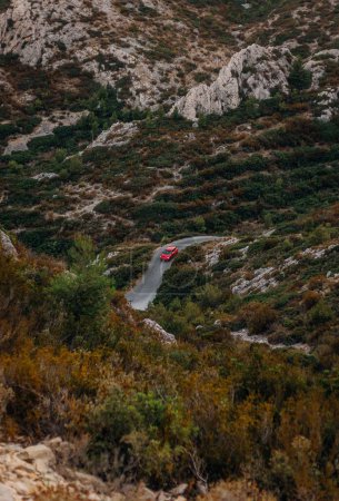 Photo for A vertical shot of a red car on the road through rocks covered with lush greenery in the Massif des Calanques - Royalty Free Image