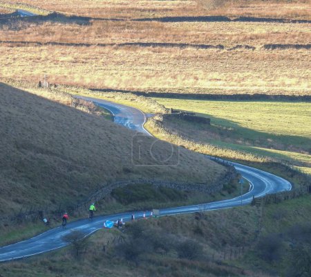 Téléchargez les photos : Une route en haut des collines sèches avec des cyclistes à vélo dessus - en image libre de droit