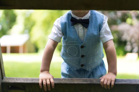 Téléchargez les photos : Un petit garçon appuyé sur une clôture tout en portant un nœud papillon mignon - en image libre de droit