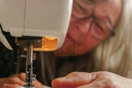 Téléchargez les photos : Older woman with white hair out of focus sewing a white fabric on a sewing machine - en image libre de droit
