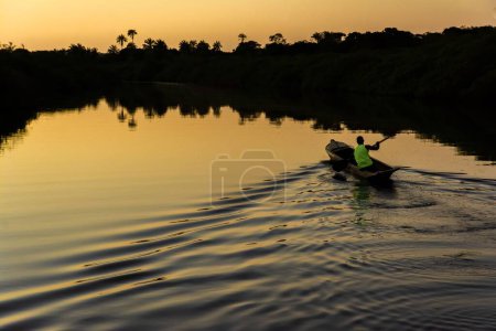 Photo for A fisherman paddling his canoe on the Jaguaripe River, City of Aratuipe, at sunset. - Royalty Free Image