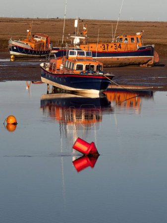Téléchargez les photos : Un port avec des bateaux de sauvetage et des bouées réfléchies sur l'eau par une journée ensoleillée - en image libre de droit