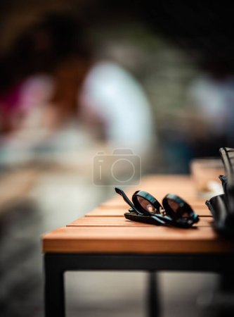 Foto de Una toma vertical de gafas de sol y billetera de cuero sobre una mesa al aire libre con fondo borroso - Imagen libre de derechos