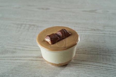 Foto de Un primer plano de la taza de tarta de queso con una superficie marrón y una barra de chocolate sobre un fondo de madera - Imagen libre de derechos