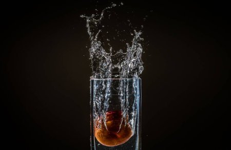 Foto de El agua salpicando de un vaso con una manzana en ella aislada sobre un fondo negro - Imagen libre de derechos