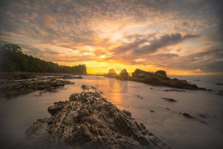 Téléchargez les photos : Les formations rocheuses uniques sur la plage sablonneuse Tanjung Layar sous fond de ciel nuageux sombre - en image libre de droit