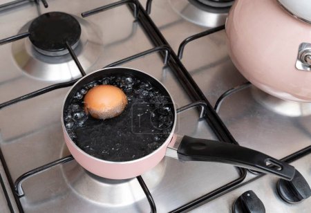 Foto de Un huevo de gallina hirviendo en una olla de metal en una estufa de gas - Imagen libre de derechos