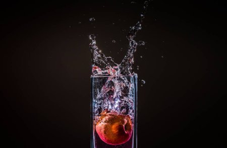 Foto de El agua salpicando de un vaso con una manzana en ella aislada sobre un fondo negro - Imagen libre de derechos