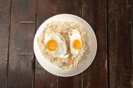 Photo for A top view shot of a rice dish with fried eggs on it, served on a white plate on a wooden table - Royalty Free Image