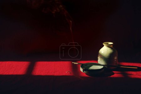 Téléchargez les photos : Fumée provenant d'un bâton d'encens dans un plateau de porcelaine caché dans l'ombre montrant le concept de méditation, de pleine conscience et de bien-être mental - en image libre de droit