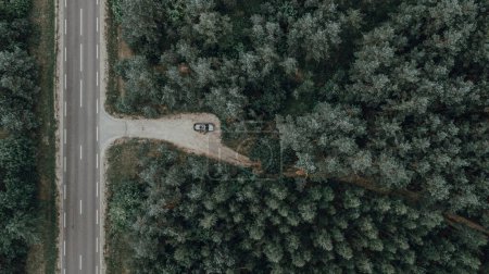 Téléchargez les photos : Une vue de dessus d'une voiture garée dans une forêt verte dense avec un sentier étroit qui la traverse - en image libre de droit