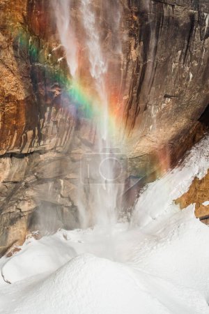 Foto de Una vertical de un hermoso arco iris arrojado sobre los acantilados en un paisaje nevado - Imagen libre de derechos