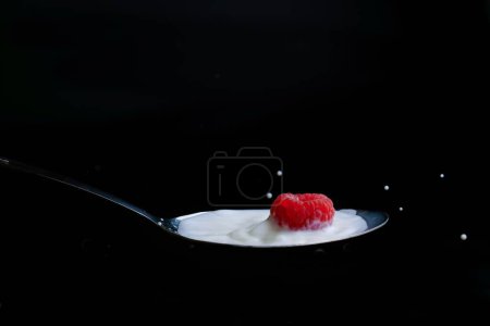 Foto de Frambuesa salpicadura de leche en una cuchara de metal efecto salpicadura con fondo negro - Imagen libre de derechos