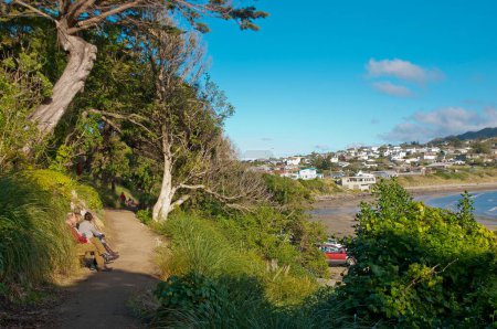 Téléchargez les photos : Trois personnes assises le long d'un chemin au-dessus de la baie de Titahi dans la ville de Porirua près de Wellington, Nouvelle-Zélande - en image libre de droit