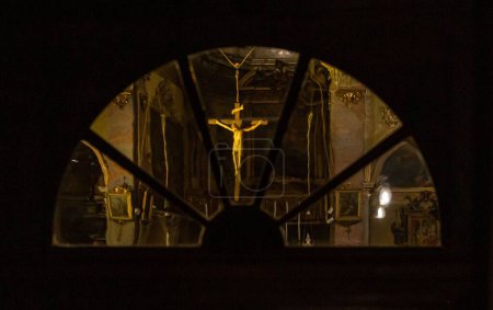 Photo for A figure of Jesus Christ on a cross hanging in a church captured from behind a glass window - Royalty Free Image