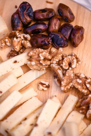 Photo for A vertical closeup shot of date palms, walnuts, and sliced cheese on the wooden surface as appetizers - Royalty Free Image