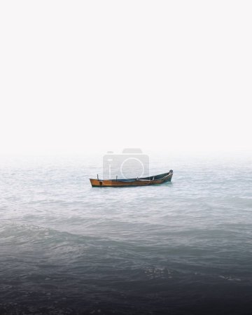 Photo for A vertical shot of a lone boat on the sea waves covered in the fog - great for wallpapers - Royalty Free Image