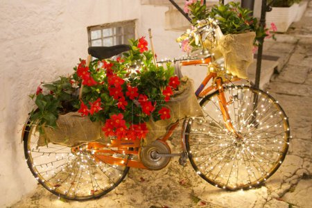 Foto de Una bicicleta decorada con flores y luces apoyadas en la pared blanca - Imagen libre de derechos