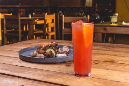 Photo for A closeup of delicious saucy chicken wings on a plate next to a refreshing drink on a wooden table - Royalty Free Image
