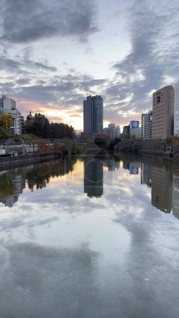 Foto de Un plano vertical de río con reflejo de edificios modernos bajo la puesta del sol cielo nublado - Imagen libre de derechos