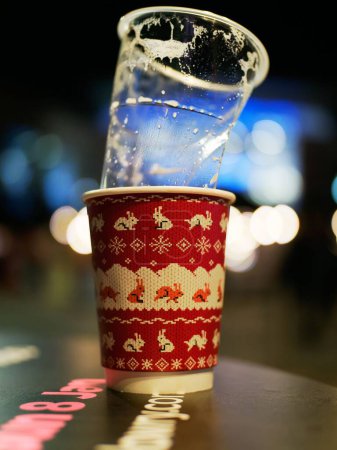 Téléchargez les photos : Un plan vertical d'une tasse de bière vide en plastique sale sur une tasse en papier sur le thème de Noël sur une table - en image libre de droit