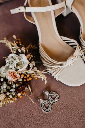 Photo for A closeup of female shoes, earrings and dry flowers on a brown surface - Royalty Free Image