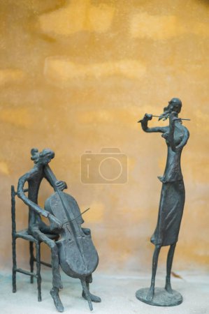 Foto de Un plano vertical de dos esculturas tocando violonchelo y violín sobre un fondo amarillo - Imagen libre de derechos