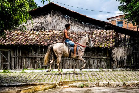 Téléchargez les photos : Un jeune homme à cheval passe devant une façade d'un magasin de céramique dans la ville d'Aratuipe, Bahia. - en image libre de droit