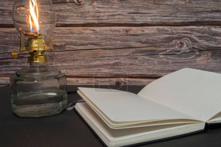 Téléchargez les photos : Un gros plan d'une vieille lampe à huile d'ouragan antique en feu avec livre ouvert sur une table en bois - en image libre de droit