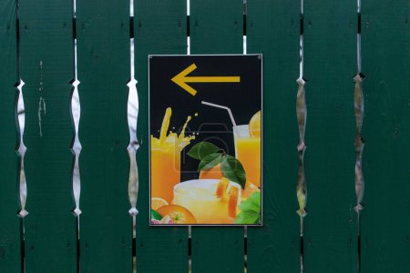 Foto de Un cartel con zumo de naranja fresco y una flecha amarilla sobre una valla de madera verde - Imagen libre de derechos