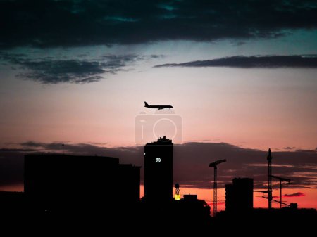 Téléchargez les photos : Une silhouette des bâtiments sous un avion volant au ciel rouge couchant - en image libre de droit