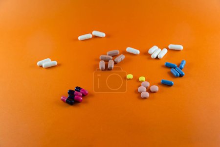 Foto de Diferentes píldoras dispersas sobre un fondo naranja. Material médico. - Imagen libre de derechos