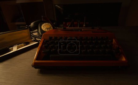 Foto de Un primer plano de una máquina de escribir antigua y teléfono en la parte superior de un escritorio en una habitación oscura - Imagen libre de derechos