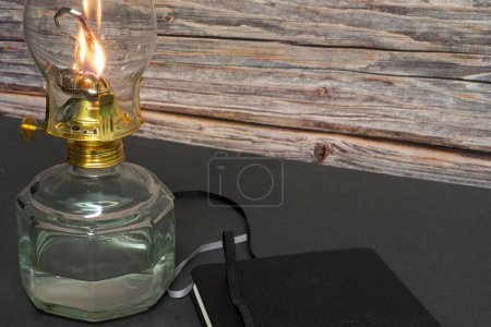 Foto de Un primer plano de una vieja lámpara de aceite de huracán antigua en llamas con libro cerrado en la mesa de madera - Imagen libre de derechos