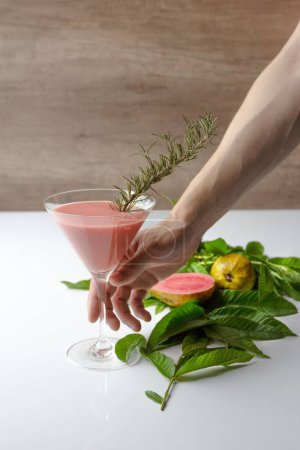 Téléchargez les photos : Plan vertical d'une personne tenant un verre à cocktail de jus de goyave - en image libre de droit