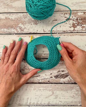 Foto de Una vista superior de las manos de una mujer con clavos pintados tejiendo una bola de hilo verde - Imagen libre de derechos