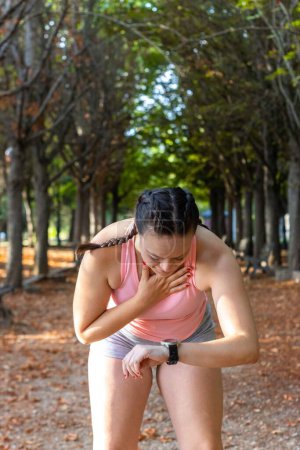 Téléchargez les photos : Plan vertical d'une jeune femme sportive faisant de l'exercice et regardant sa montre dans un parc - en image libre de droit