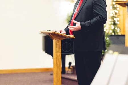 Foto de Un macho vestido con un traje negro y predicando aferrado a un púlpito - Imagen libre de derechos