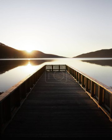 Téléchargez les photos : Un plan vertical du lever du soleil lors d'une promenade sur une jetée en bois avec la silhouette des montagnes en arrière-plan en Norvège - en image libre de droit