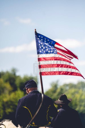 Foto de Un disparo vertical de un soldado sosteniendo la bandera de Estados Unidos durante el desempeño militar en la recreación de la guerra civil en la ciudad de Jackson, Michigan, EE.UU. - Imagen libre de derechos
