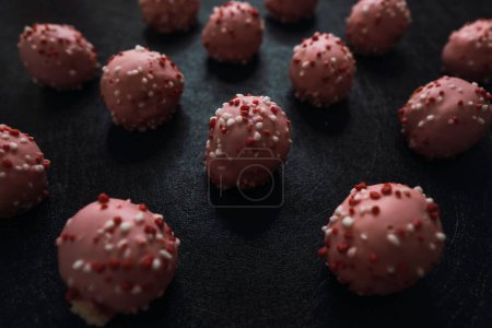 Téléchargez les photos : Un gros plan de délicieuses boules de gâteau rose avec glaçage coloré isolé sur un fond sombre - en image libre de droit