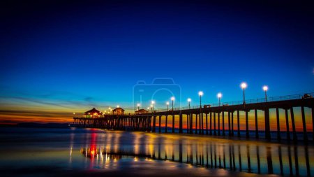 Téléchargez les photos : Une vue panoramique de Huntington Beach Pier au-dessus de la mer reflétant les lumières colorées au coucher du soleil - en image libre de droit