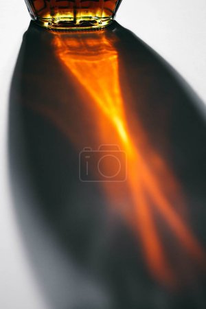 Téléchargez les photos : Bouteille de sirop d'érable canadien brun foncé réfléchissant sur fond blanc créant une forme abstraite avec une lumière orange - en image libre de droit