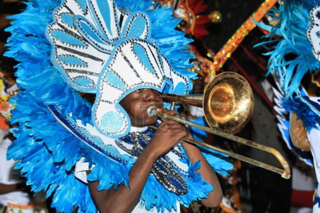 A man playing trombone in a traditional costume during a Junkanoo parade in the Bahamas.