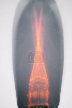 Foto de Frasco de jarabe de arce canadiense marrón oscuro que refleja sobre fondo blanco creando una forma abstracta con luz naranja - Imagen libre de derechos